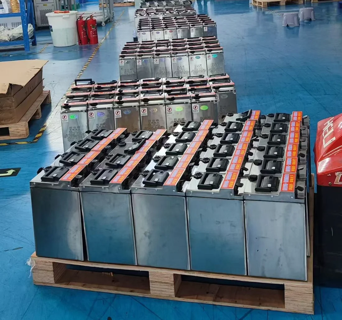 Rows of metal battery enclosures with handles and connectors on workshop pallets